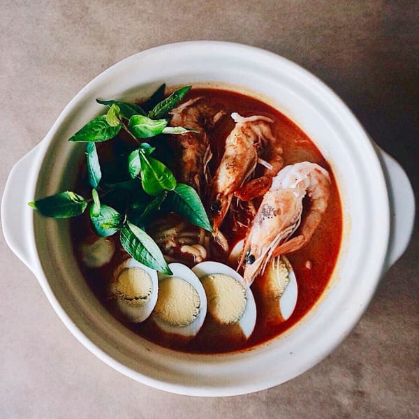 Shiok Singapore Kitchen's laksa with prawns, sliced hard-boiled eggs, and fresh basil in a white bowl.