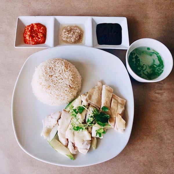Hainanese chicken rice with three dipping sauces and a bowl of green soup on a white plate.
