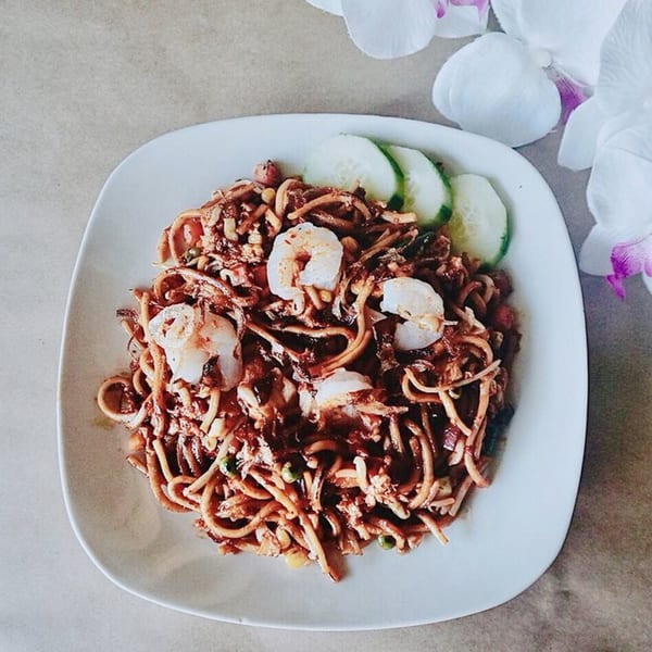A plate of dark sauced noodles with shrimp and cucumber slices, garnished with white orchids.